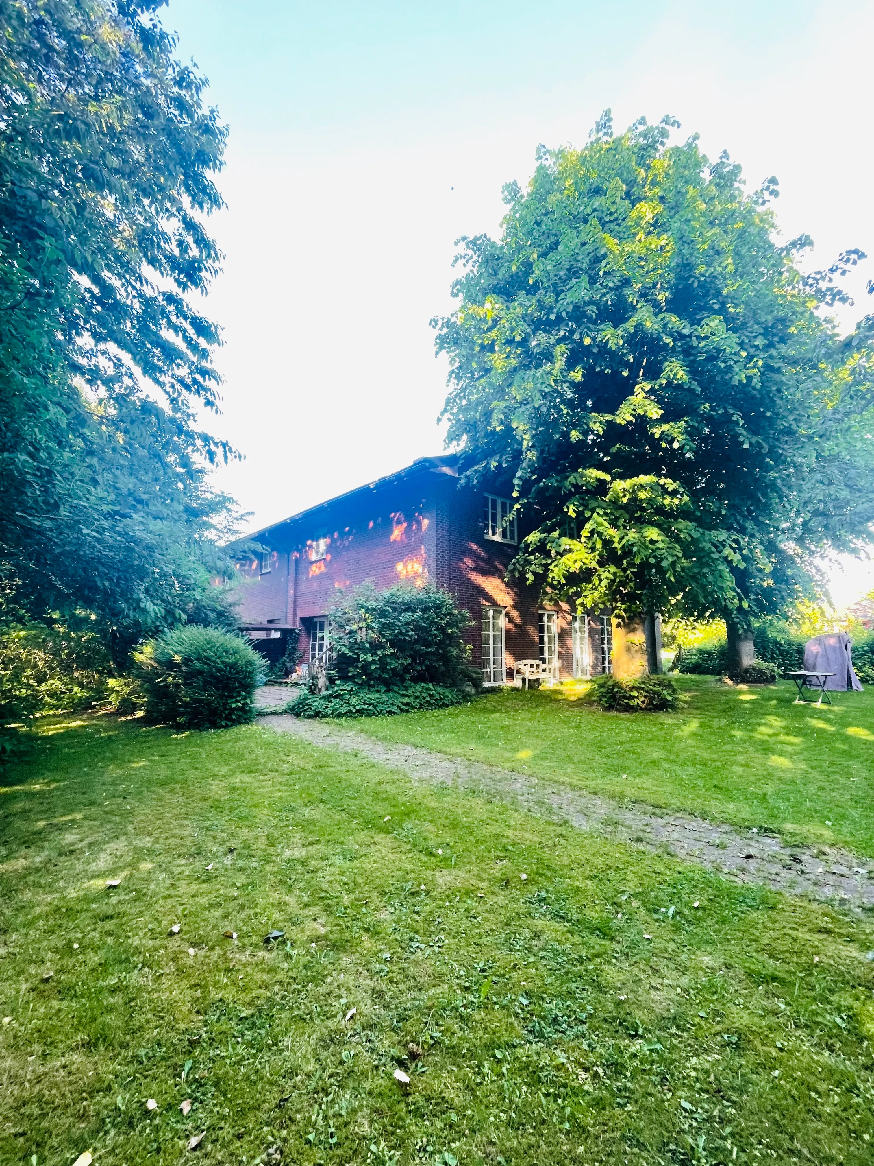 Ein Ziegelhaus mit großen Bäumen und einem gepflegten Rasen davor.